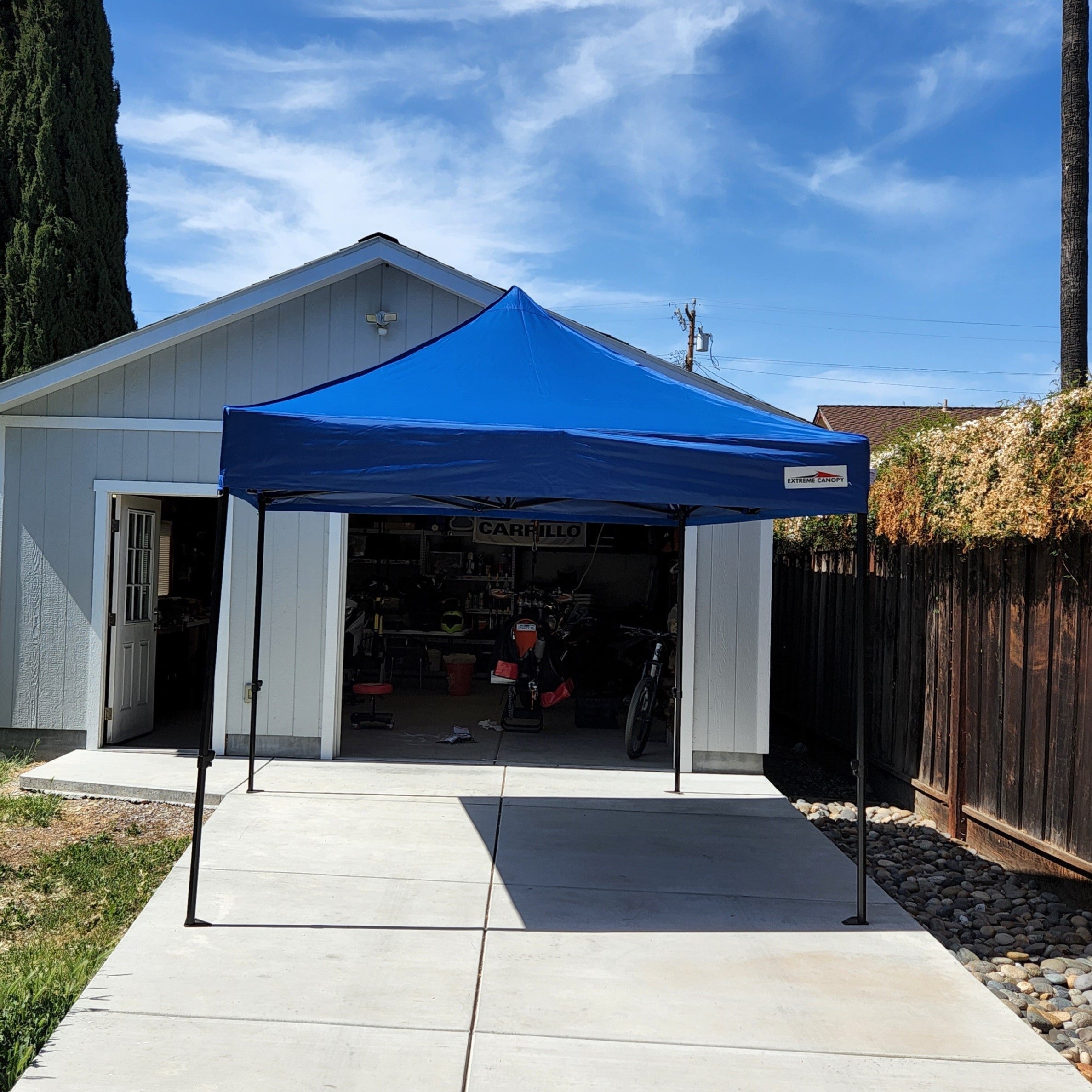Blue pop-up marquee set up in front of a garage with a clear blue sky.
